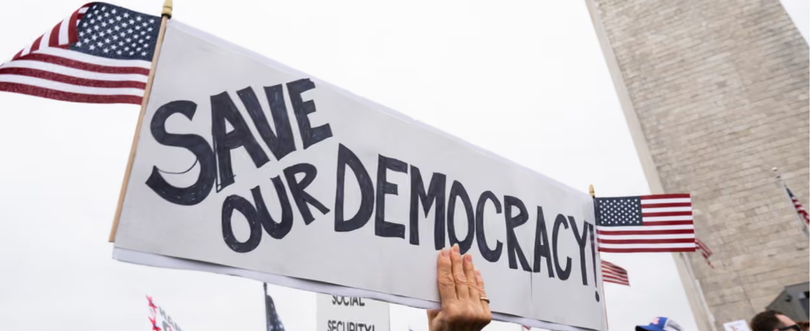 Protesters holding a hand-lettered Save Our Democracy sign with American flags near the Washington Monument